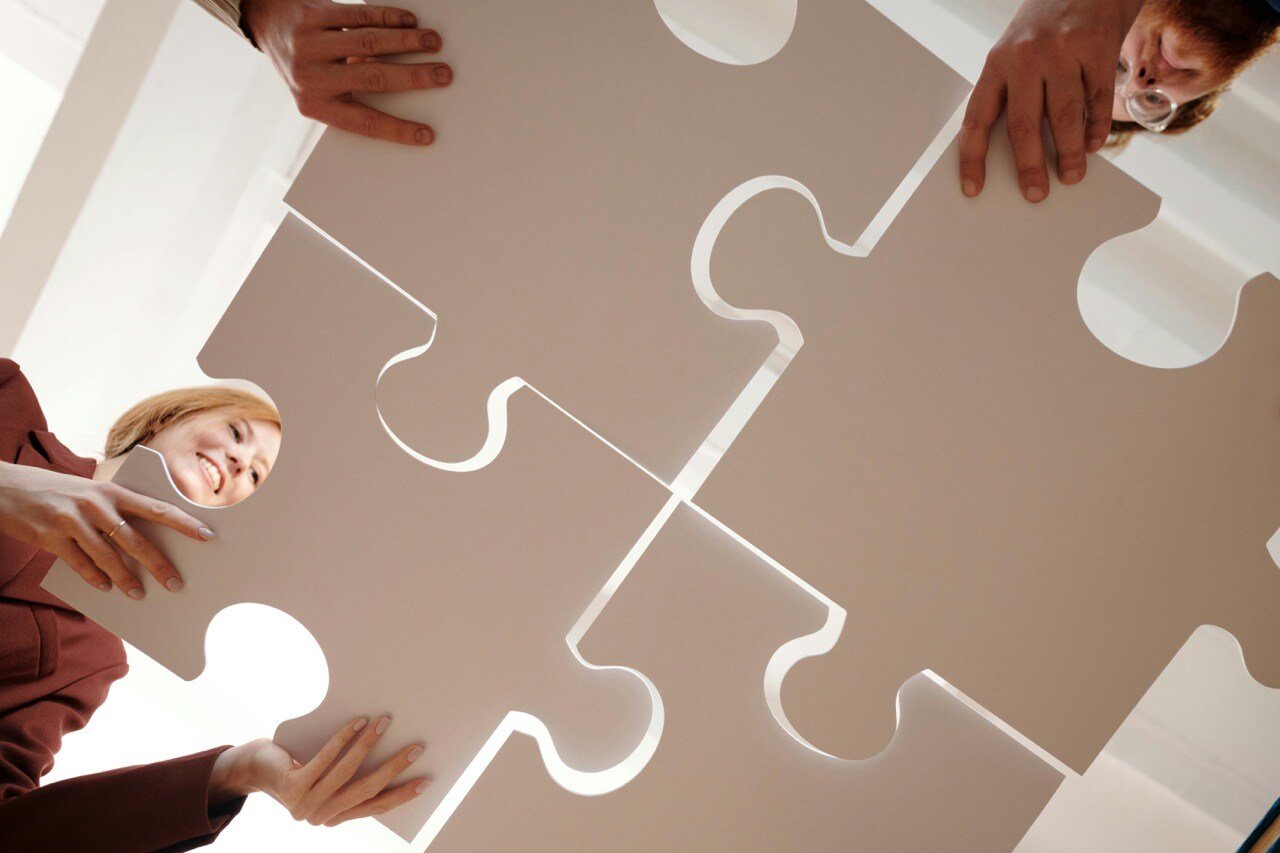 Four people holding large puzzle pieces and putting them together to fit.