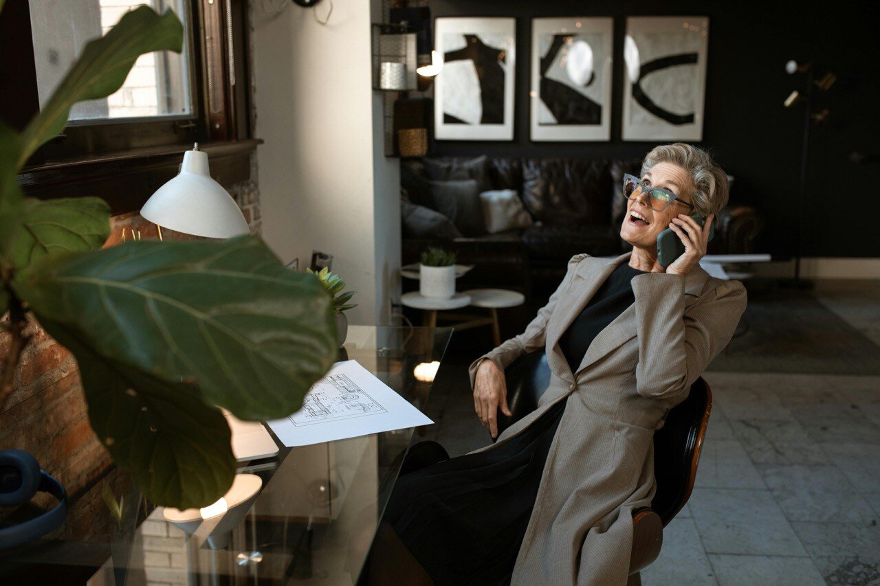 Business woman sitting in office chair conducting phone interview in large modern office.