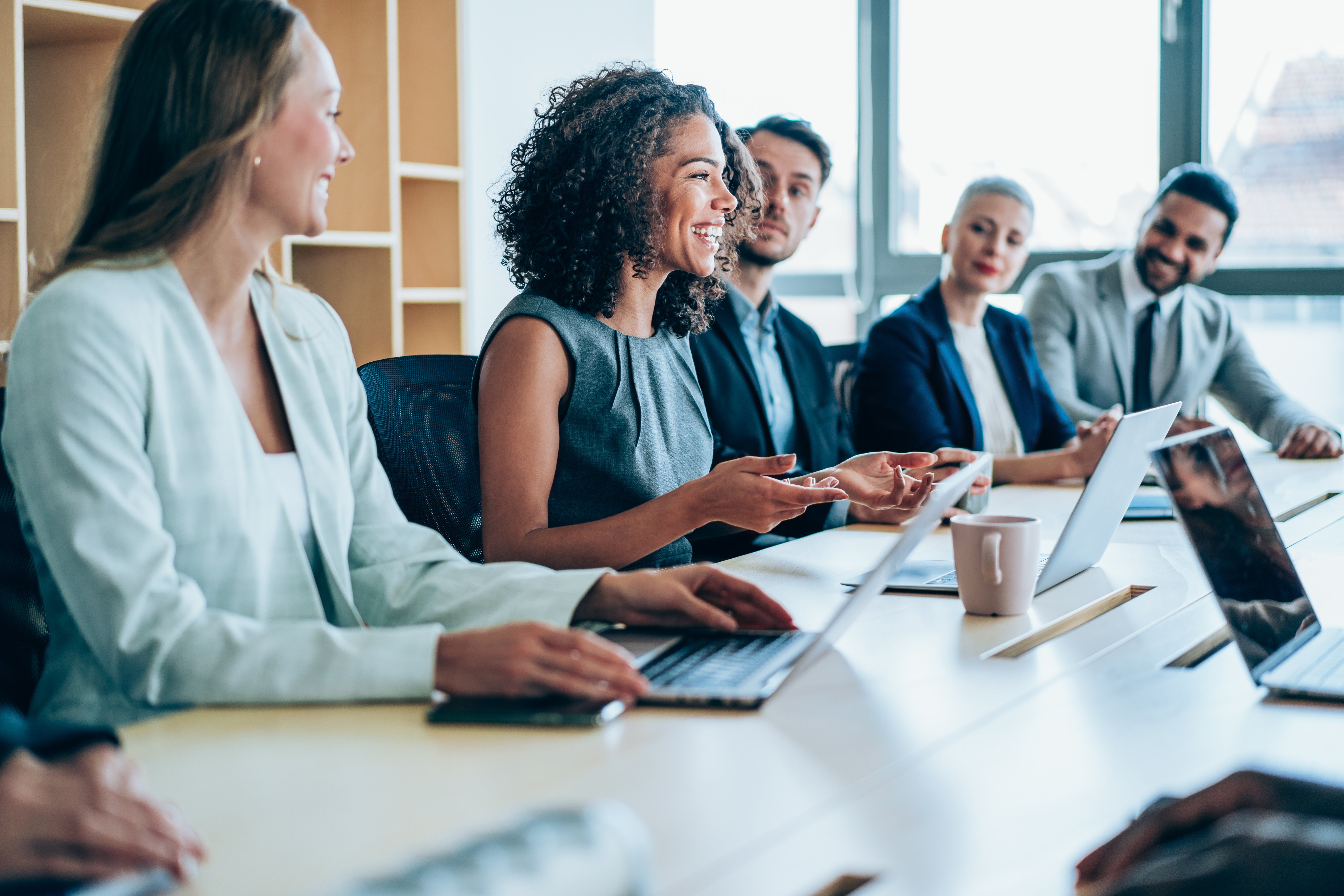 Professional team members meeting at conference table smiling with emphasis on woman in middle.