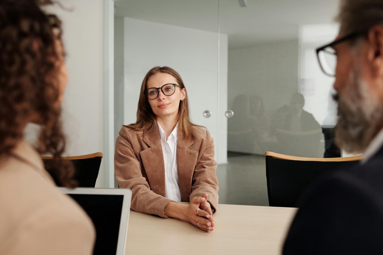 Young professional sitting across table from two business professionals in modern office during interview process.